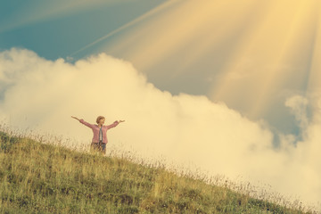 Young girl holds hands up against the sky and hillside
