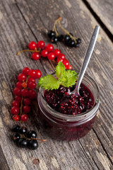 berry jam in a glass jar and fresh red currants on wooden board