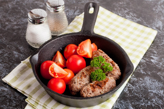 sausages in a frying pan on black background. Fresh tomate.