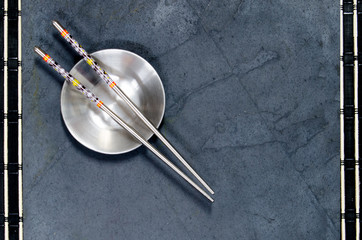 Stainless steel chopsticks and bowl on black slate