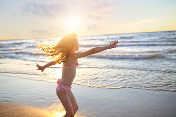 Fototapeta na wymiar happy little girl with curly long hair dancing in a swimsuit during sunset