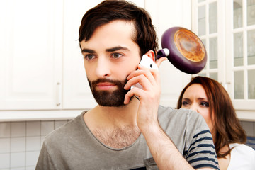 Angry young woman hitting men with frying pan.