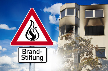 Schild mit Brandanschlag und Brandstiftung vor ausgebranntem Haus
