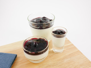 The tasty homemade blueberry panna cotta (Italian pudding dessert) in the small glass on wooden board.