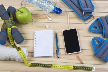 Sport Equipment. Dumbbells,  Ankle Weights, Wrist Weights, Towel, Tape Measure, Bottle Of Water, Smart Phone With Earphones And Notebook To Workout Plan On Wooden Table. Sport Fitness Background