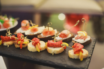 Beautifully decorated catering banquet table with different food snacks and appetizers with sandwich, caviar, fresh fruits on corporate christmas birthday party event or wedding celebration