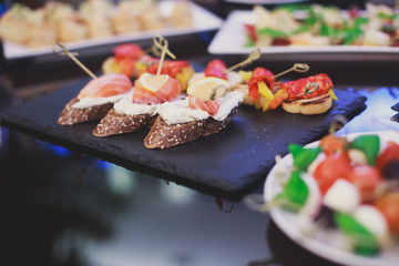 Beautifully decorated catering banquet table with different food snacks and appetizers with sandwich, caviar, fresh fruits on corporate christmas birthday party event or wedding celebration