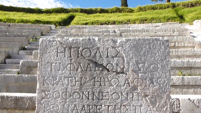 Closeup of Greek inscription with an ancient Greek theatre in the background