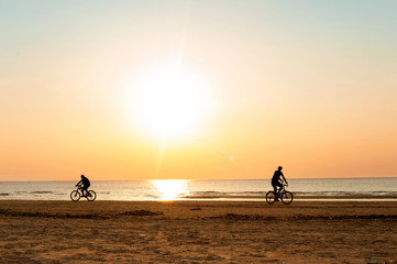 Men cyclists silhouettes at summertime sunset background on the