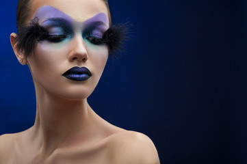No limits for fantasy. Studio shot of a female model wearing creative makeup with blue eye shadows and blue lipstick and feather attachments