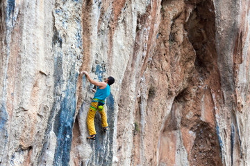 Fototapeta premium Mature Rock Climber ascending steep colorful rocky Wall Lead Climbing
