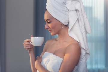 Naked woman with towel on her head and body drinking herbal tea after bath.