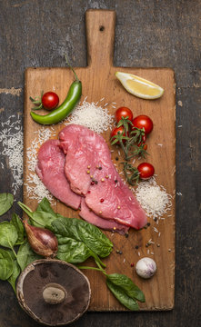 raw pork on a cutting board with hot peppers, herbs and lemon on wooden rustic background top view close up