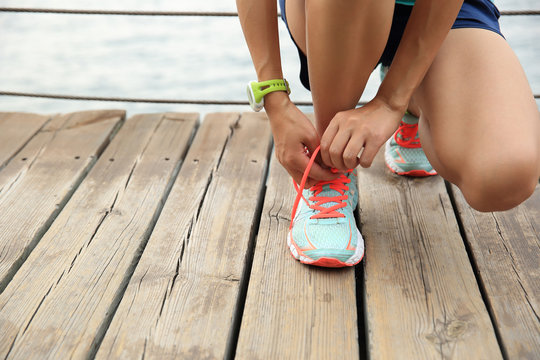 sports woman runner tying shoelace on wooden boardwalk seaside
