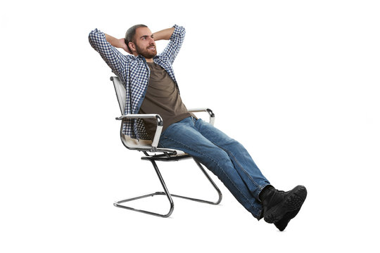 Shot Of A Young Man Leaning Back In A Chair With His Hands Behind His Head Isolated On White