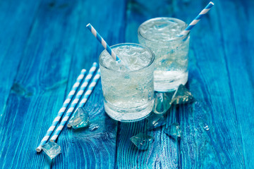 
cold sparkling mineral water with ice in a glass on a blue wooden background