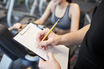 close up of trainer hands with clipboard in gym
