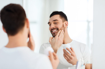 happy young man applying cream to face at bathroom