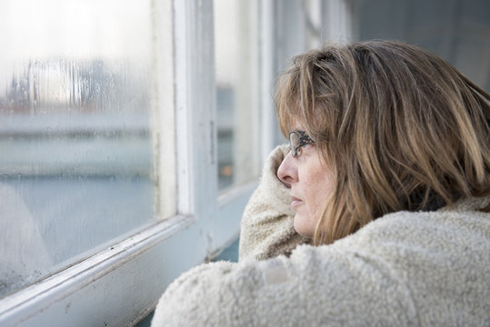 Portrait Image Of A Fed Up Mature Woman Looking Out Of The Window On A Rainy Miserable Day