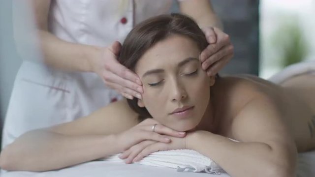 Young beautiful woman is getting a relaxing head and face massage in wellness center. Shot on RED Cinema Camera.