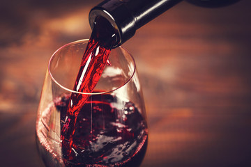 Pouring red wine into the glass against wooden background - obrazy, fototapety, plakaty