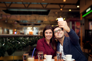 Happy young couple taking selfie with smart phone at cafe in mall. Copy space for your text. Shallow depth of field. Very useful photo for processing with one click on edit image.