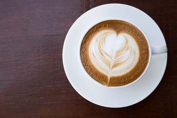 Cup of hot coffee latte with heart shaped foam art on wood backg