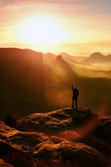 Man takes photos with smart phone on peak of rock empire. Dreamy fogy landscape, spring orange in a...