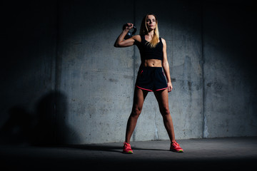 Athletic woman posing with kettlebell against concret wall
