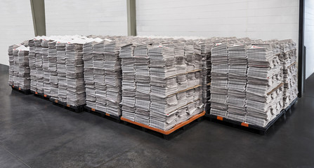 Multiple stacks of newspapers on pallets in warehouse ready to be delivered.