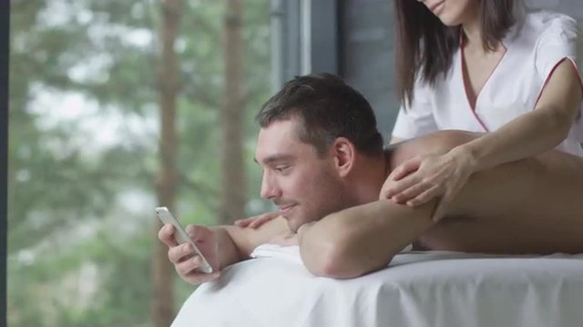 Handsome man is using a smartphone during a relaxing massage in wellness center. Shot on RED Cinema Camera.