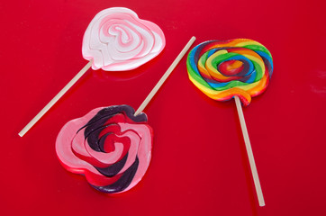 Three colorful heart shaped suckers or lollipops on a red background