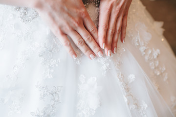 Hands bride with manicure on background of white dress