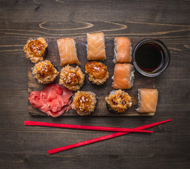 Philadelphia sushi roll with salmon and baked sushi with crab with ginger and soy sauce and red chopsticks on wooden rustic background top view close up