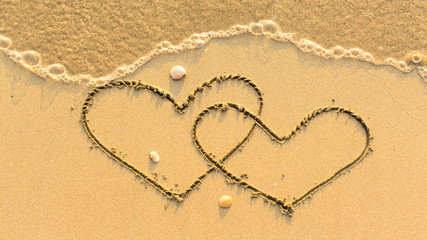 Fototapeta na wymiar Two hearts drawn on the sand beach with the soft wave. Honeymoon concept.