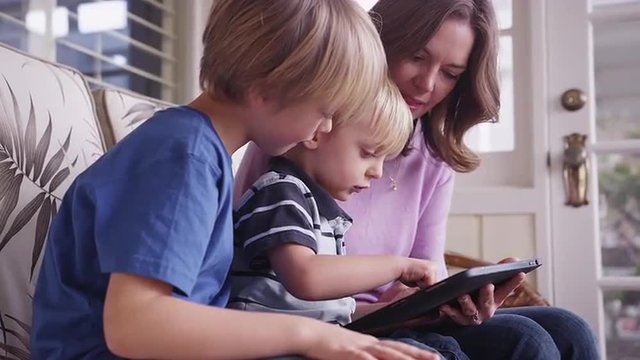 Mother teaching her young boys how to use an ebook tablet