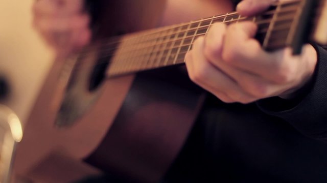 Man's hands playing acoustic guitar by mediator. Fretboard focus in out.