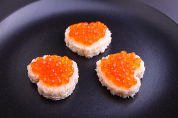 sandwich with red caviar in a heart shape on a black plate