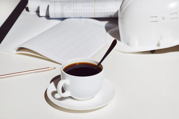 workplace architect. A cup of coffee, a helmet and blueprints on white table.