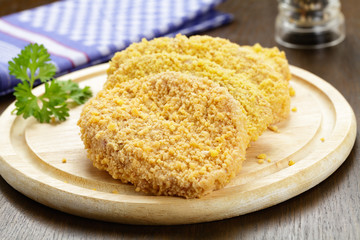 Panierte rohe Schnitzel auf einem Holzbrett