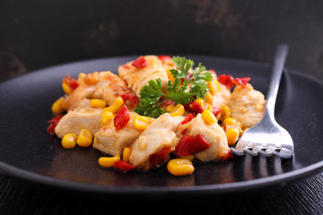 fried chicken with corn and sweet red peppers on a black plate
