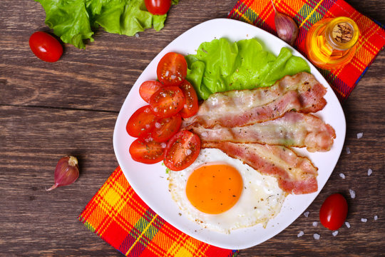Hearty breakfast. Fried egg with bacon and tomatoes on a wooden background