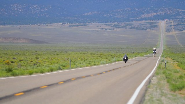 A motorcycle rides down a long highway in rural Nevada.