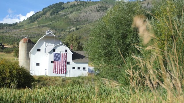 An American flag waves on the side of a picturesque white barn in the mountains outside of Park City, Utah.