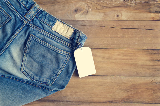 Blue jeans with white blank tag on wooden background