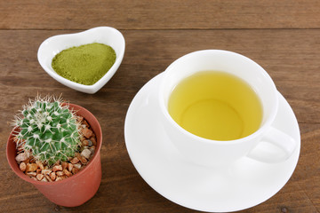 Obraz na płótnie Canvas The Japanese matcha green tea powder on ceramic heart shaped bowl and cup of hot green tea and little cactus in plant pot on wooden planks.