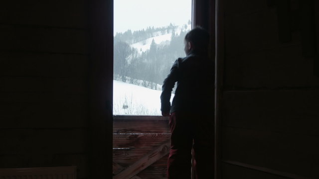 The child looks at snow through a window
