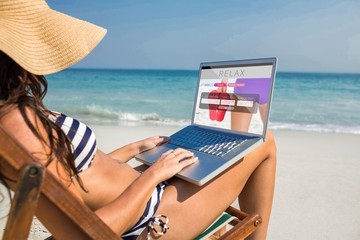 Composite image of pretty brunette using laptop on deck chair