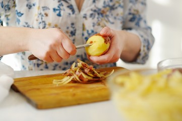 Young woman peeling potatoes with a knife.