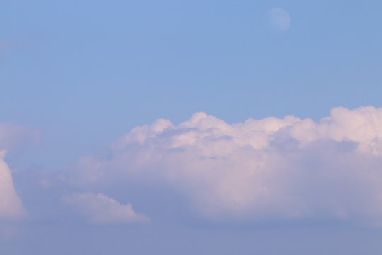 Big white tufted cloud in blue sky and moon during summer day